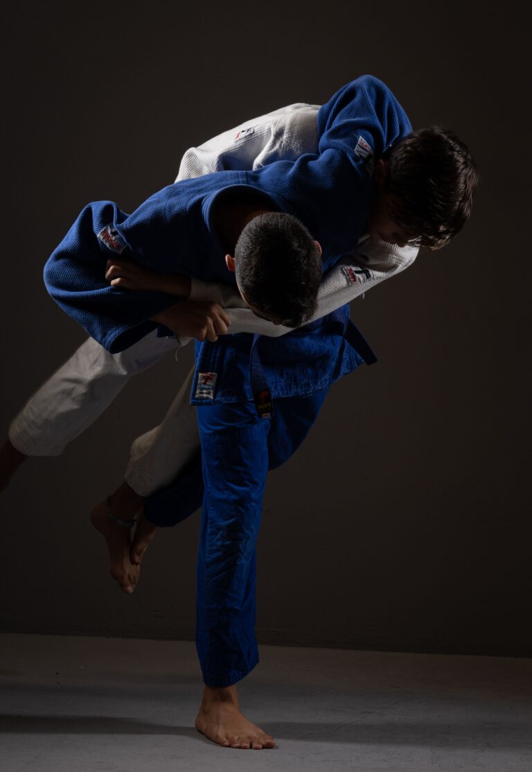 Unrecognizable young barefooted male judoists in judogi fighting on ring against black background